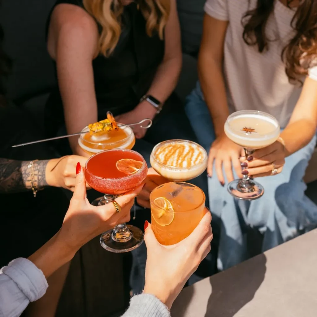 High-angle view of diverse hands holding various garnished cocktails.