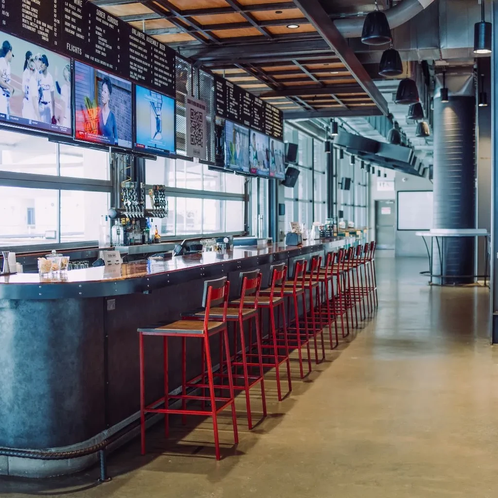 Industrial chic bar with red stools and digital menu screens.