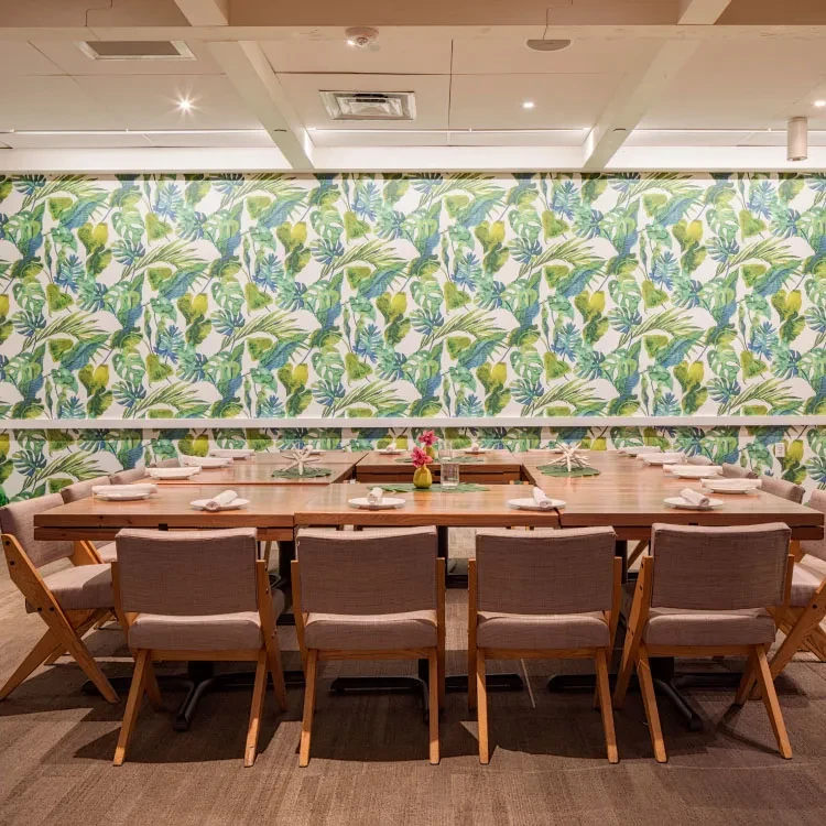 Empty restaurant dining room with large set table and tropical wallpaper.