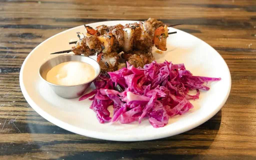 Two grilled meat skewers, purple cabbage salad, and sauce.