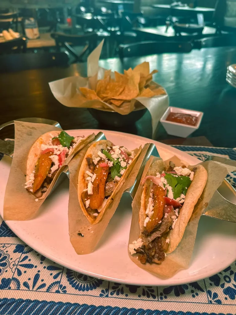 Three meat tacos with onions, cheese, and cilantro on a plate.