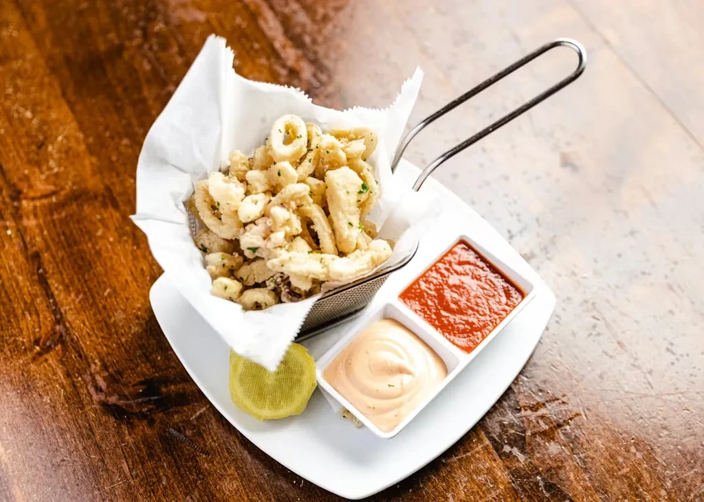 Golden fried calamari in a basket, sauces, lemon on wooden table.