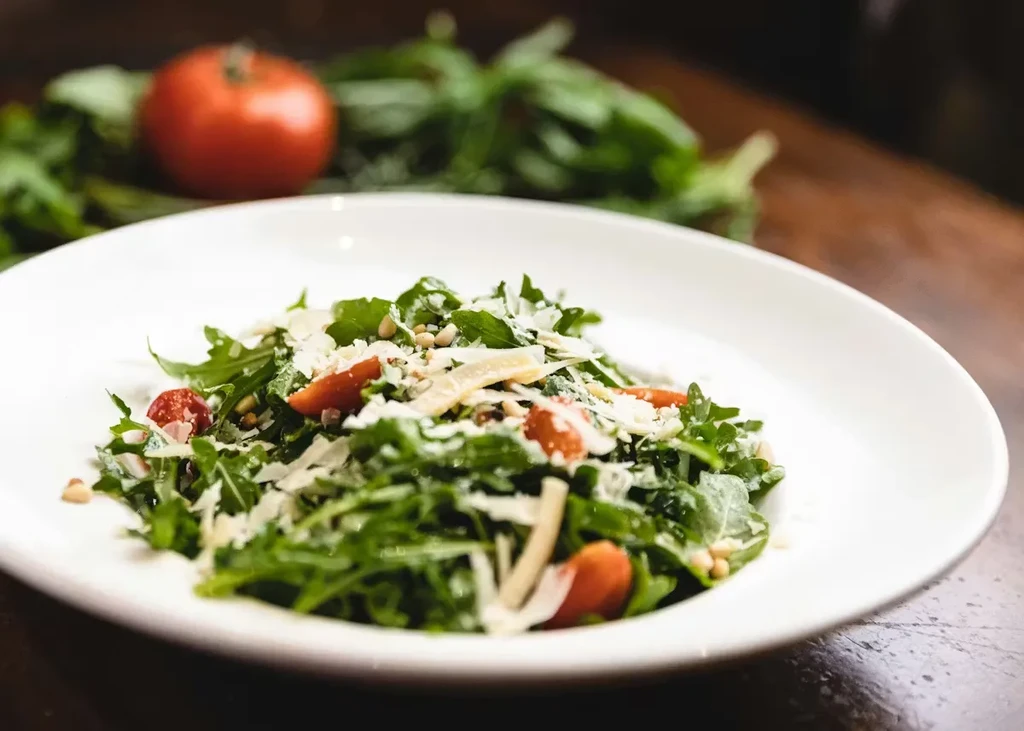 Green arugula salad with cherry tomatoes, Parmesan, and pine nuts on wood.