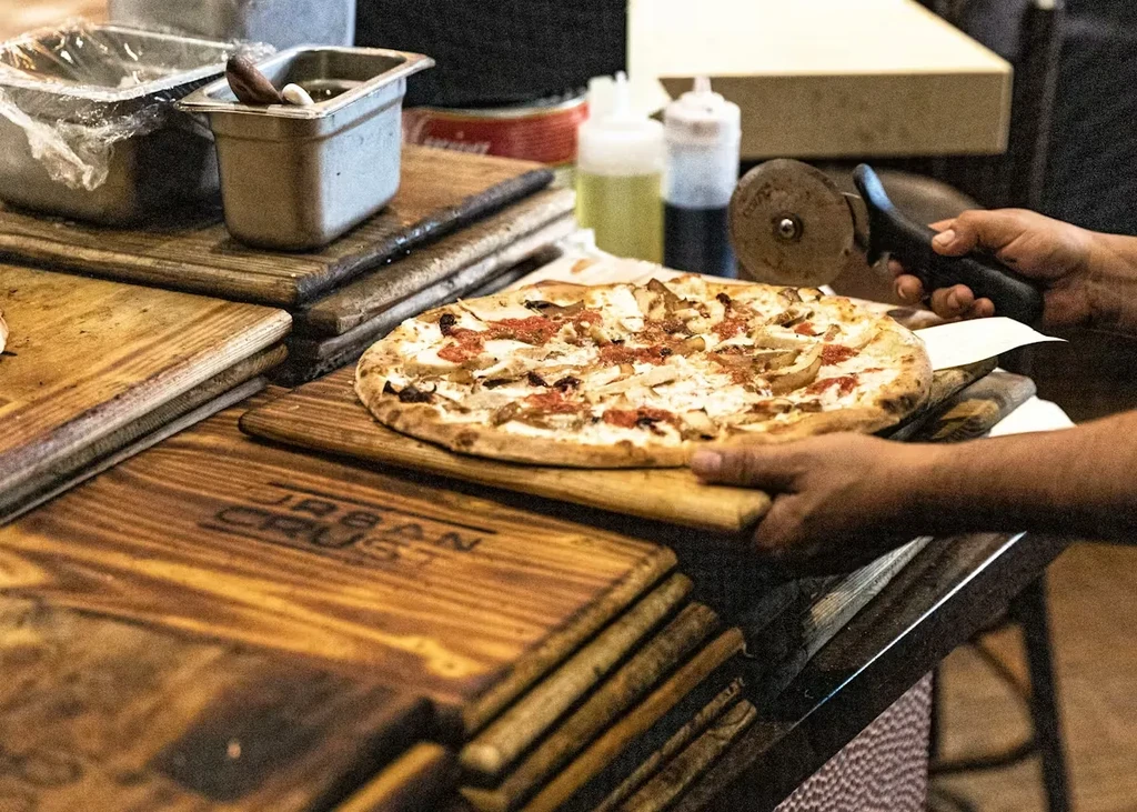 Freshly baked chicken pizza on a wooden paddle, being sliced.