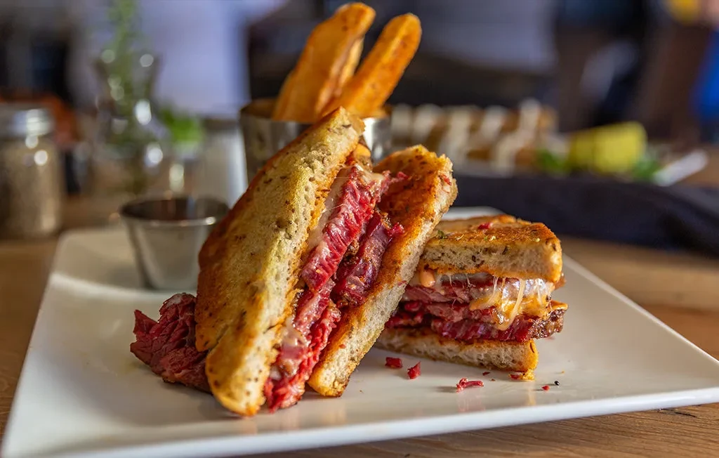 Halved grilled meat and cheese sandwich with fries in a restaurant.