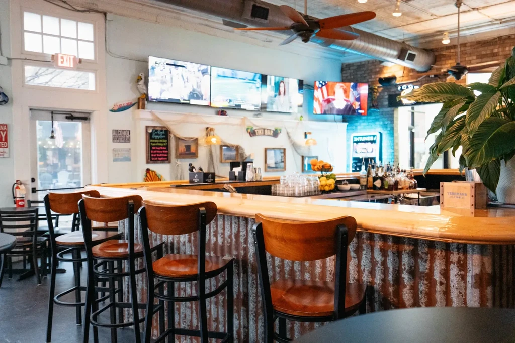 Casual bar interior with a wood counter, Tiki decor, and multiple TVs.