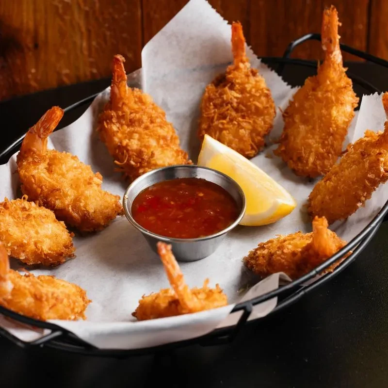 Crispy coconut shrimp with red dipping sauce and a lemon wedge.