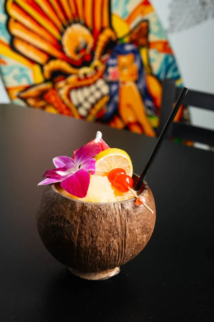 Malibu cocktail in a coconut shell with orchid, lemon, and cherries.