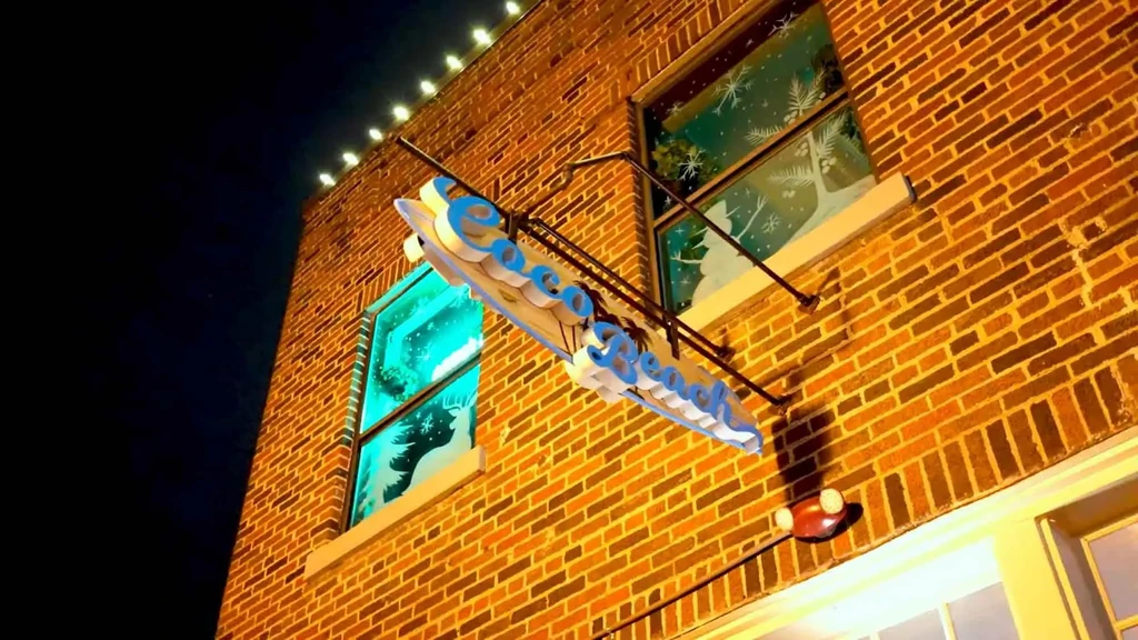 Brick building exterior at night with "Coco Beach" sign, holiday decorations.