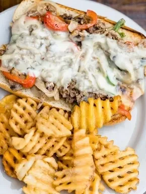 Overflowing cheesesteak sandwich with gooey cheese, onions, peppers, and waffle fries.