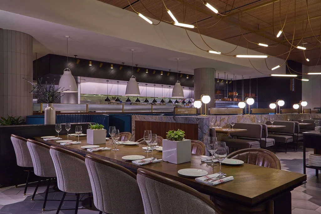 Elegant modern restaurant dining area with communal table and open kitchen.