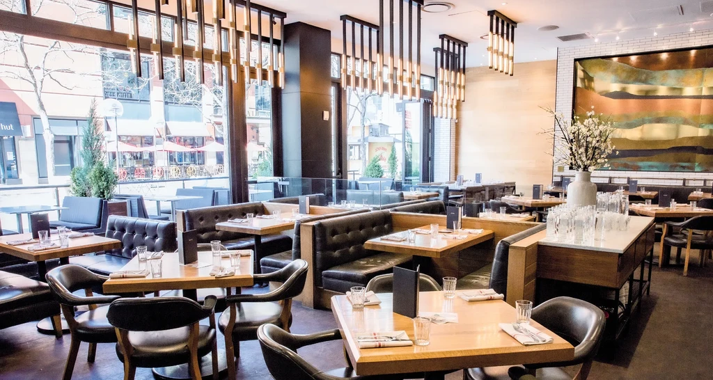 Empty upscale restaurant with booth seating, set tables, and street view.