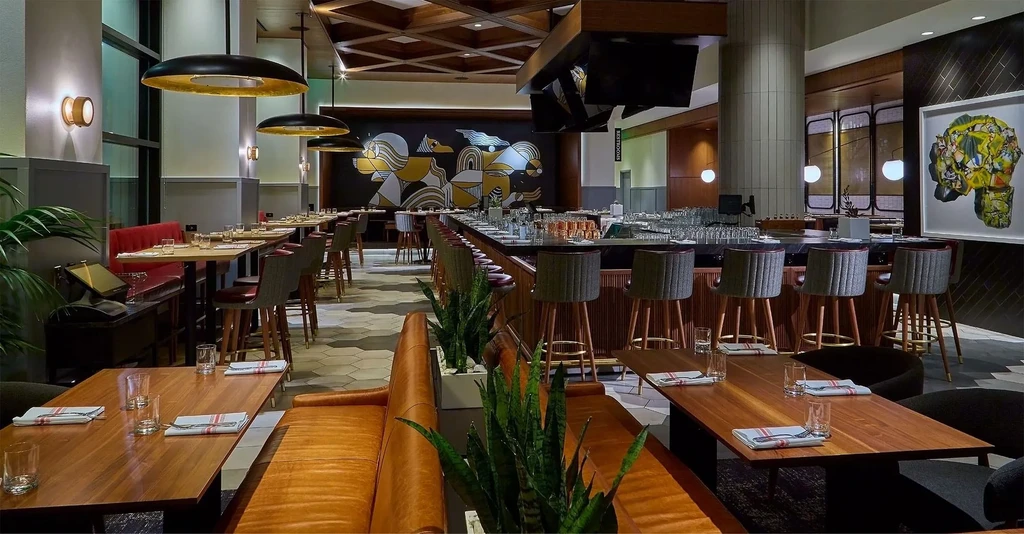 Empty modern restaurant interior with bar, tables, and warm lighting.