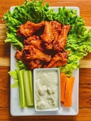 Crispy chicken wings, celery, carrots, and dip on a white plate.