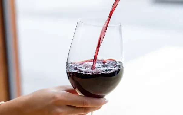 Hand holds a stemmed glass as red wine pours, splashing.