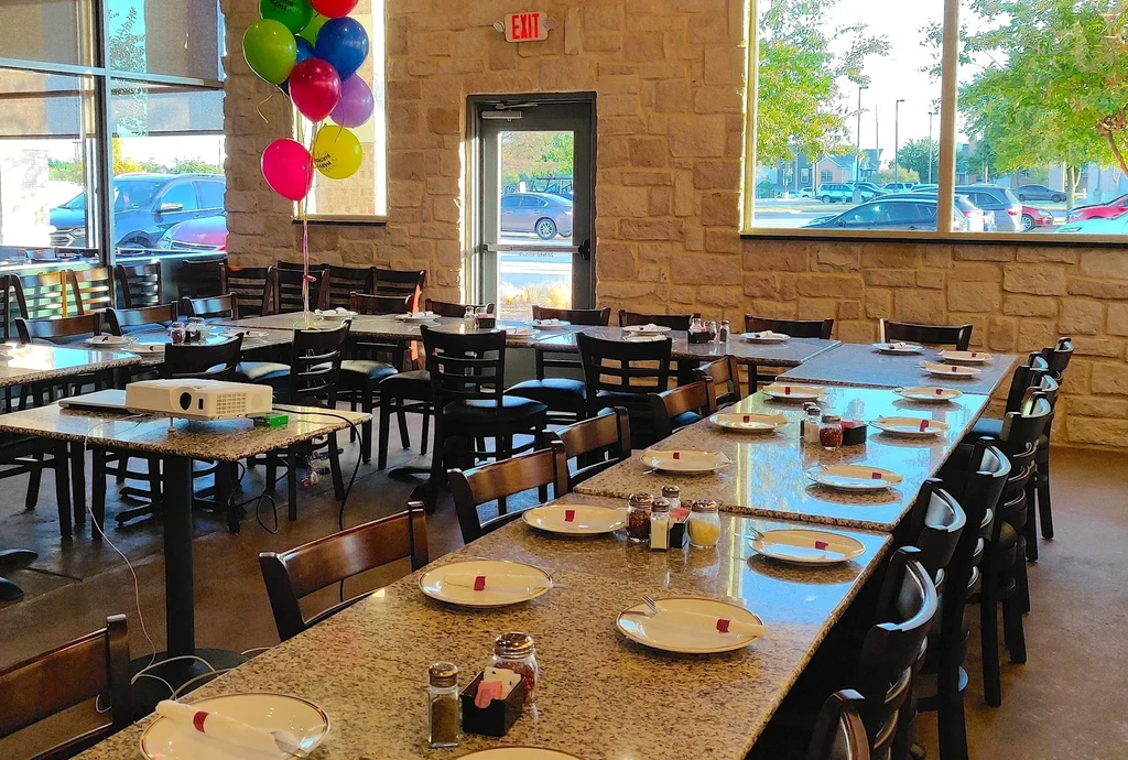 Empty restaurant event space with tables, chairs, balloons, and a projector.