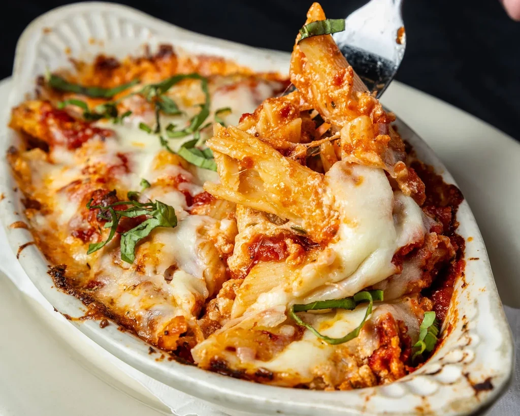 Fork lifting baked pasta with red sauce, melted cheese, and basil.