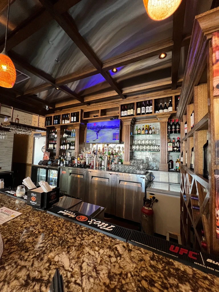 Clean, well-stocked bar interior with spirits, glasses, and golf on TV.
