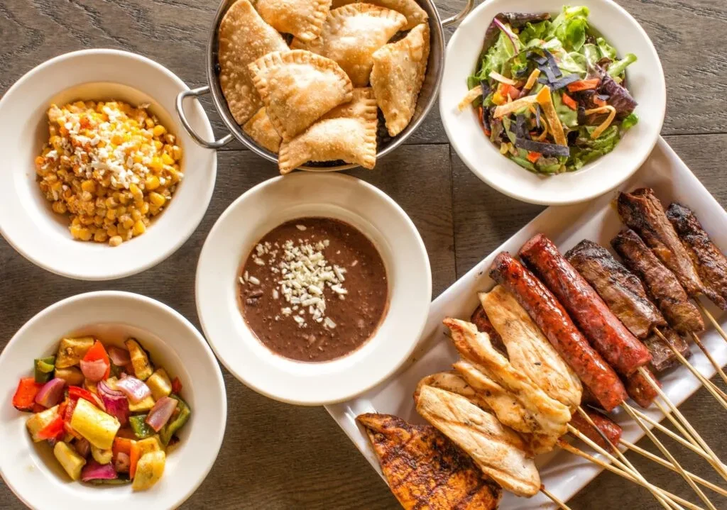 Overhead view of diverse food: bowls of sides, platter of grilled meats.