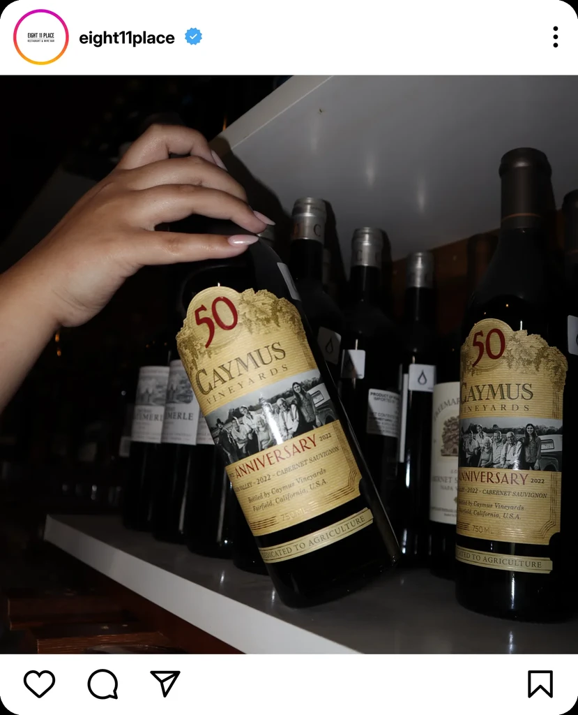 Hand placing a 2022 Caymus 50th Anniversary Cabernet Sauvignon bottle.