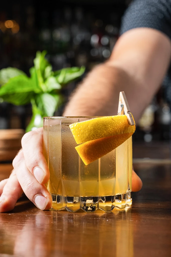 Hand holds cold amber cocktail with citrus peel garnish.