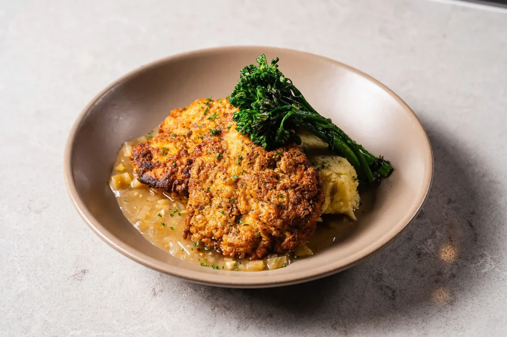 Golden-brown crispy cutlets, mashed potatoes, gravy, and broccolini in a ceramic bowl.