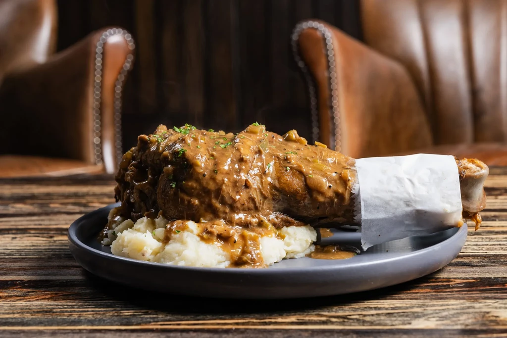 Generously portioned meat, gravy, mashed potatoes, on a wooden table.