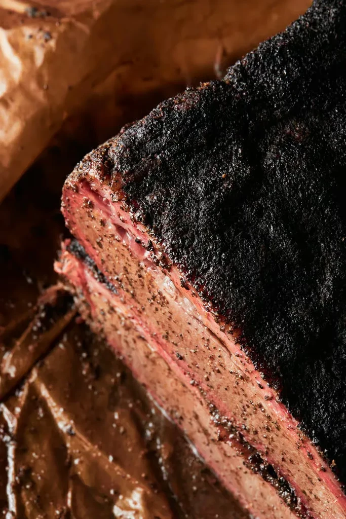 Smoked brisket cross-section, dark bark, pink smoke ring, on paper.