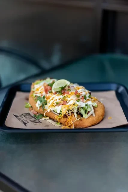 Fried bread topped with meat, cheese, lettuce, pico de gallo, and lime.