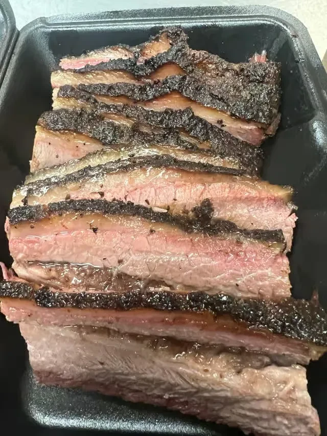 Smoked brisket slices with dark bark and pink smoke ring in container.