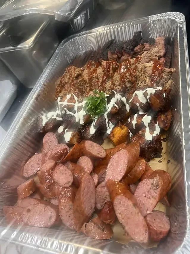 Large catering tray with shredded meats, caramelized chunks, and sausage slices.
