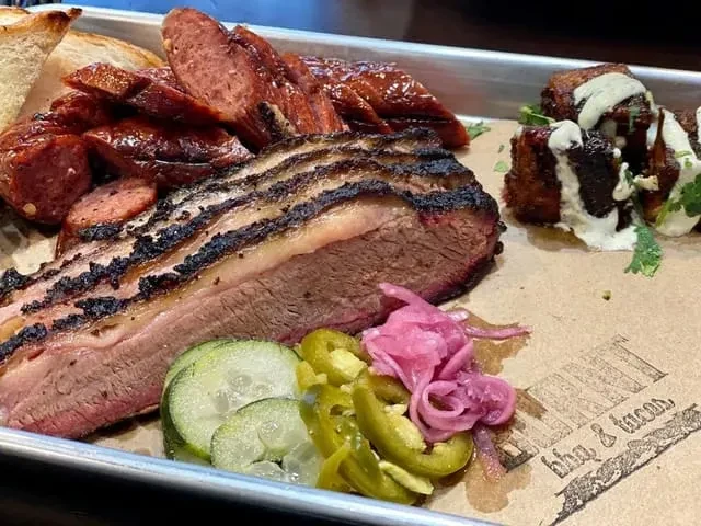 Smoked barbecue platter with brisket, sausage, burnt ends, and pickles.