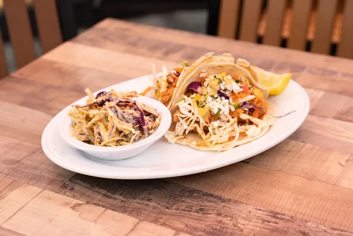 Two vibrant tacos, coleslaw, and lemon on a wooden table.