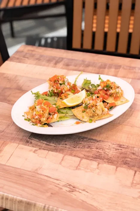 Plate of nachos with vibrant salsa, fresh herbs, and a lime.