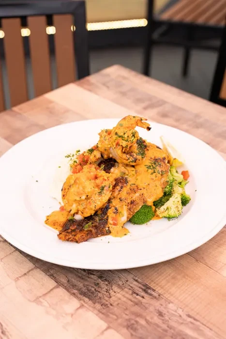 Pan-seared fish or chicken with creamy sauce, shrimp, vegetables, and lemon.