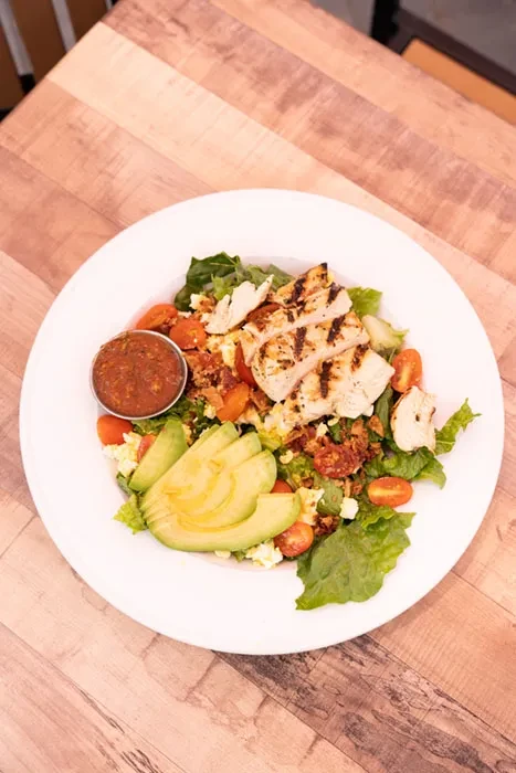 Grilled chicken and avocado salad with tomatoes, bacon, lettuce, and dressing.