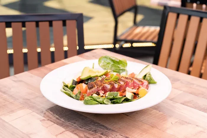 Seared tuna salad with avocado, greens, and red vegetables in a white bowl.