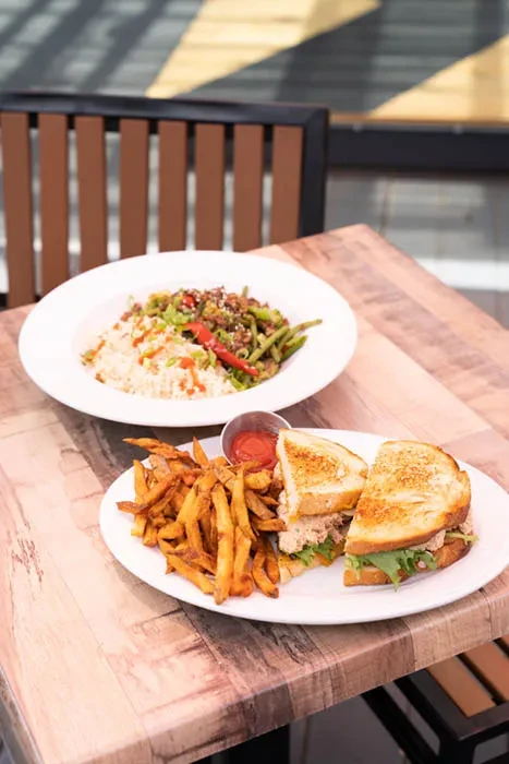 A grilled sandwich with fries and a rice dish on a rustic wooden table.