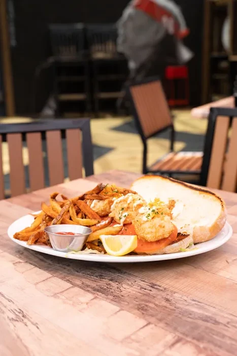 Crispy fried shrimp po'boy, fries, red sauce, and lemon wedge.