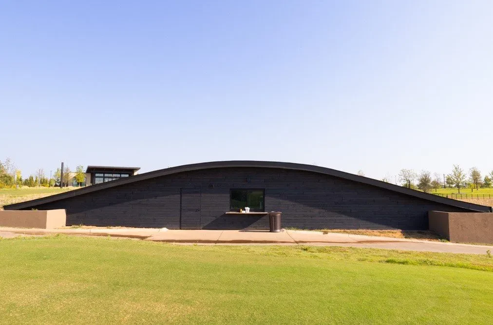 Low-profile dark building, undulating roof, service window, green lawn.