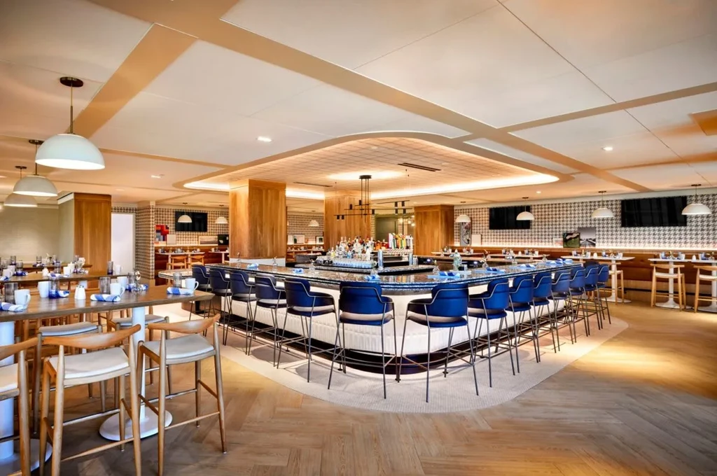 Modern restaurant interior with central bar, herringbone floor, and patterned walls.