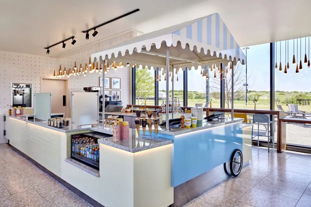 Bright, whimsical dessert counter: striped canopy, soft-serve, outdoor view.