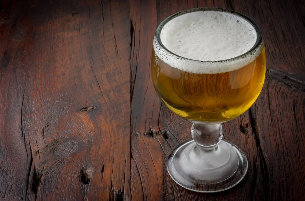Cold golden amber beer in a goblet on dark rustic wood.
