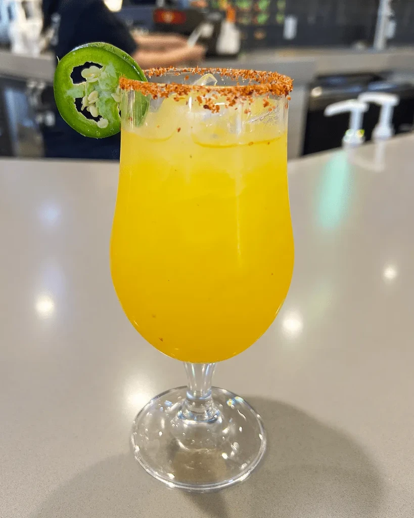 Spicy yellow drink in stemmed glass with jalapeño and chili-lime rim.