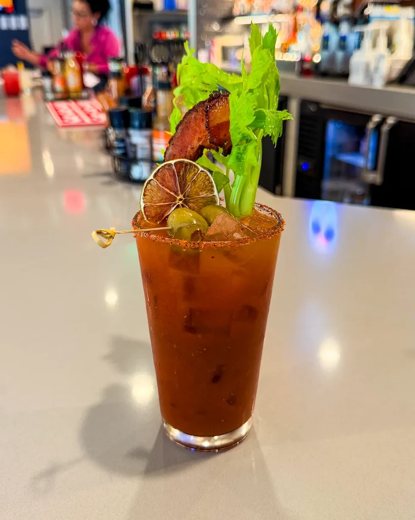 Bloody Mary cocktail elaborately garnished with celery, bacon, lime, olives.