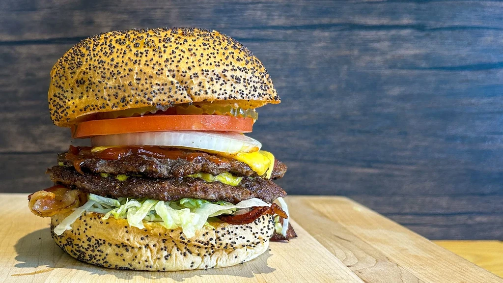 Stacked burger with two beef patties, bacon, cheese, and vegetables.