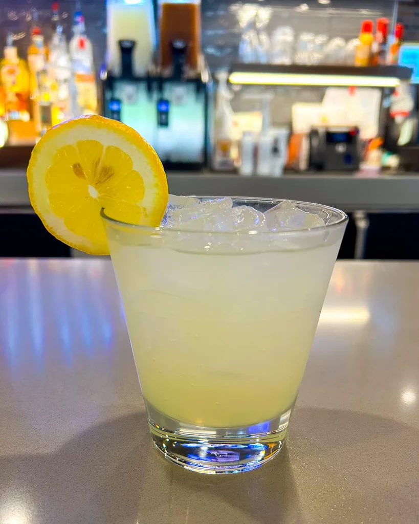 Pale yellow drink with ice and lemon slice at a bar.