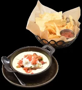 Tortilla chips, salsa, skillet of queso with meat and tomatoes.