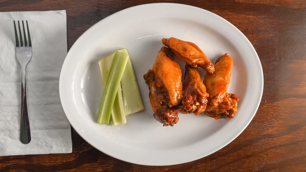 Buffalo chicken wings with celery and a fork on a wooden table.