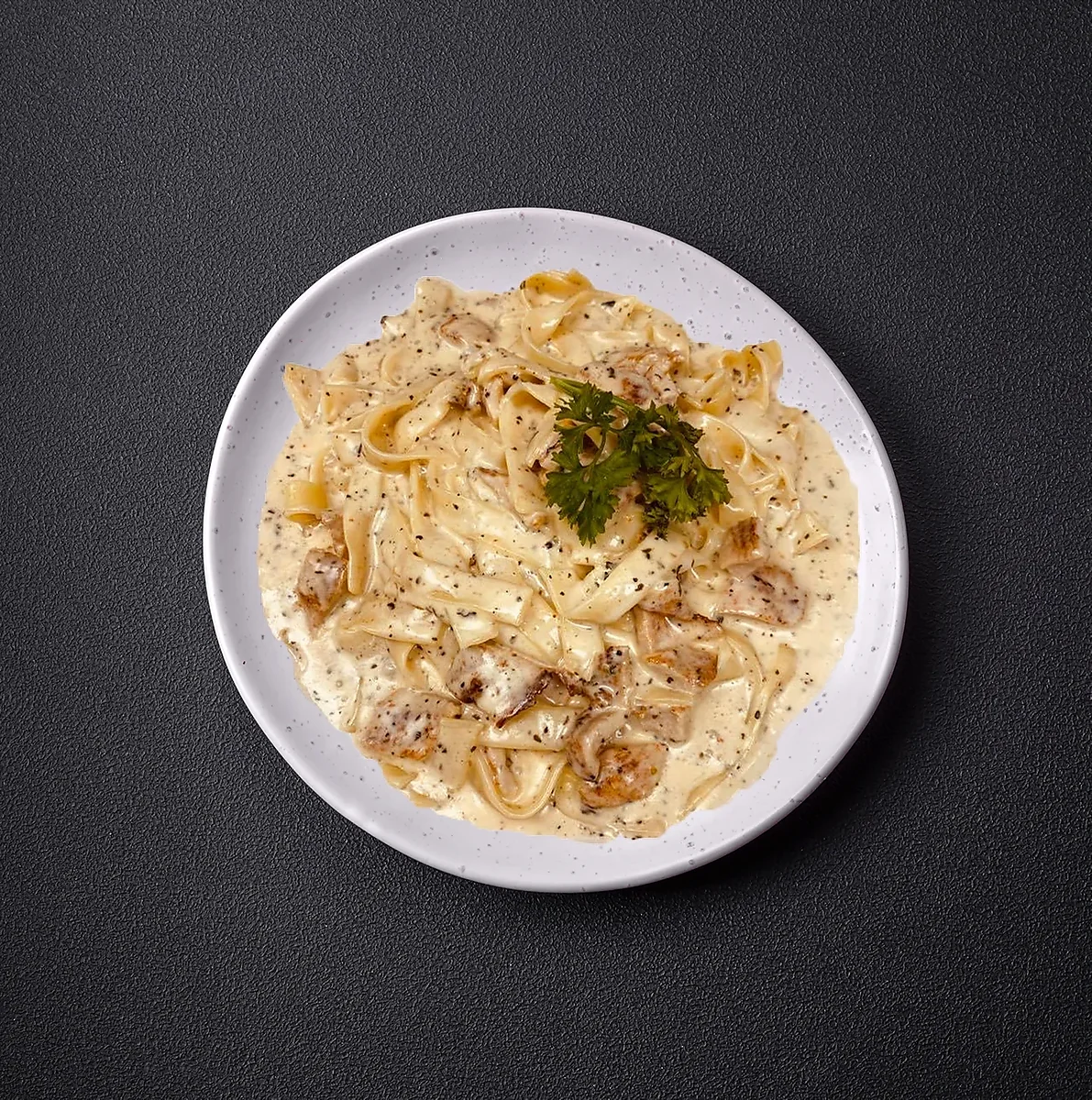 Fettuccine alfredo with grilled chicken and herbs on plate